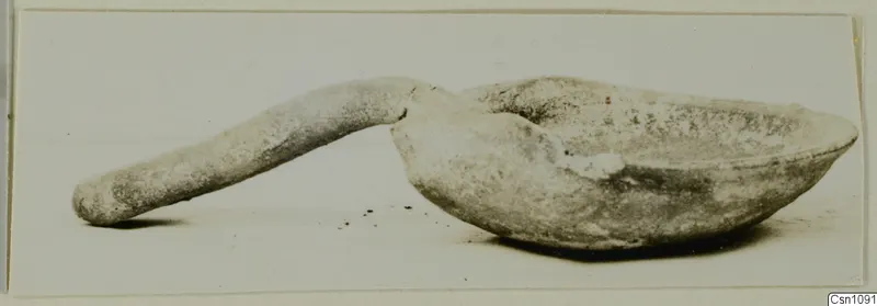 Terracotta lamp with a long solid handle and a shallow bowl, shown in side view on a pale surface.