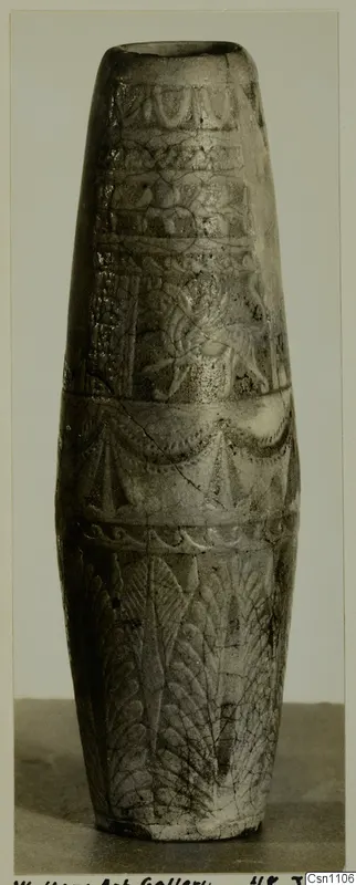 Faience pot with carved bands of pattern, tall tapering form, photographed against a grey backdrop