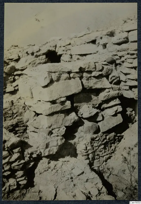 Stone wall remains on the Acropolis of Idalion, with gaps between the blocks, loose soil and scrub below.
