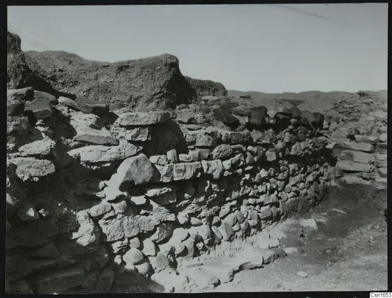 Stone wall foundations at Nitovikla, with rough stones laid in courses against a dry earth bank.