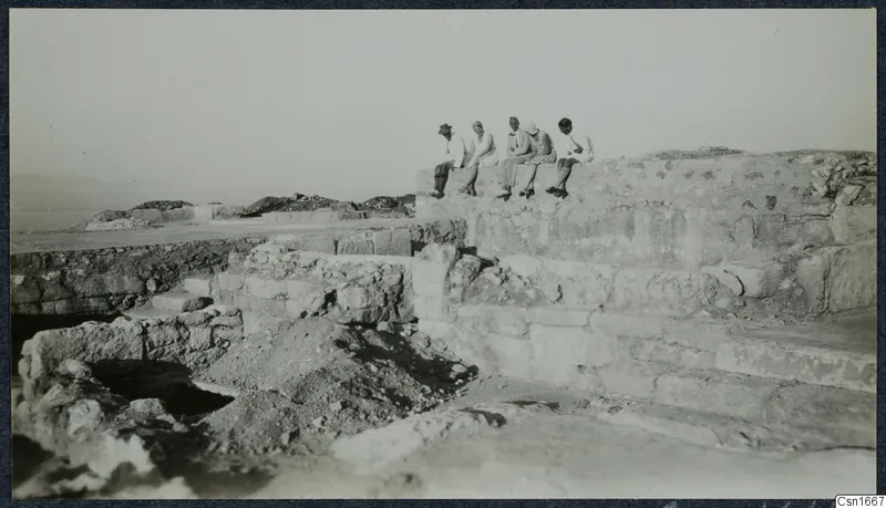 Five people sit in a row on top of a stone structure at Vouni, with cut stone courses and excavated ground below.