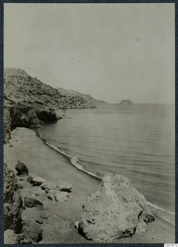 Rocky coastline with a sandy beach and calm sea at Vouni, with a small island offshore.