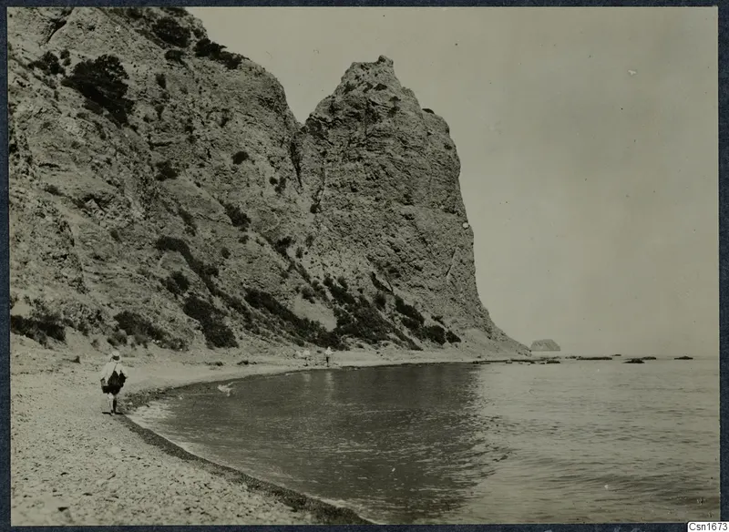 Rocky cliff above a pebble beach at Vouni, with a walking figure with a bag and calm sea to the right