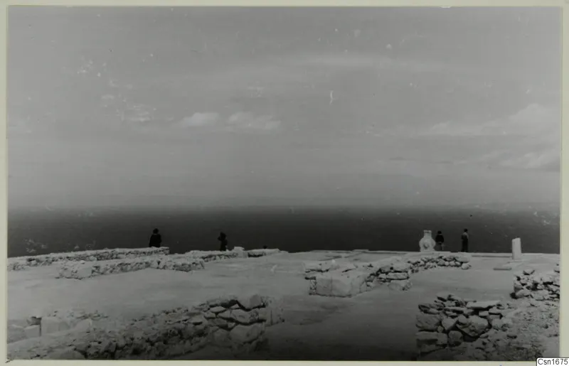 Hilltop view at Vouni Palace with low ruined walls in the foreground and four people standing near the sea edge