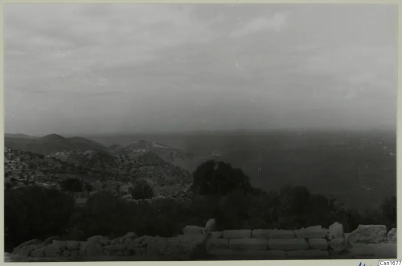View from Vouni Palace over scrubby hills and trees towards the sea, with stone wall tops in the foreground