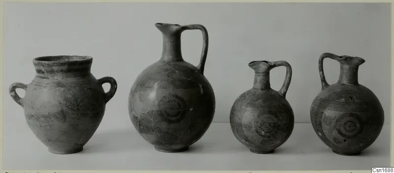 Four painted pots from Marion shown in a row against a grey backdrop, one two-handled jar and three jugs.