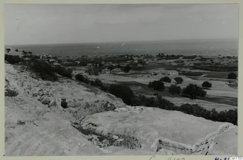 The theatre at Soli: cut stone ledges in the foreground, with a village, fields and the sea beyond