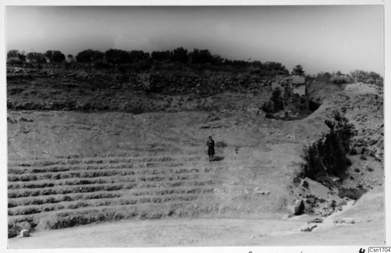 The theatre at Soli, with stepped rows cut into the slope and one standing person in the middle distance