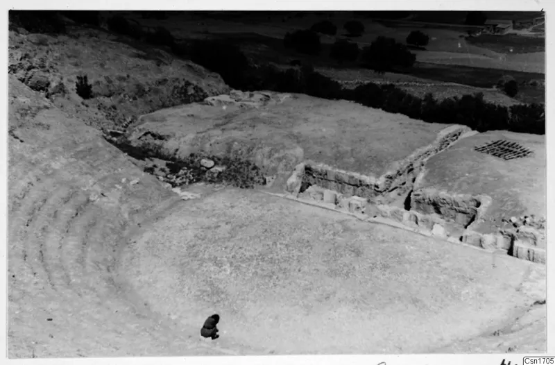 The theatre at Soli, with curved tiered seating, a stone wall with large blocks, and one small crouching figure