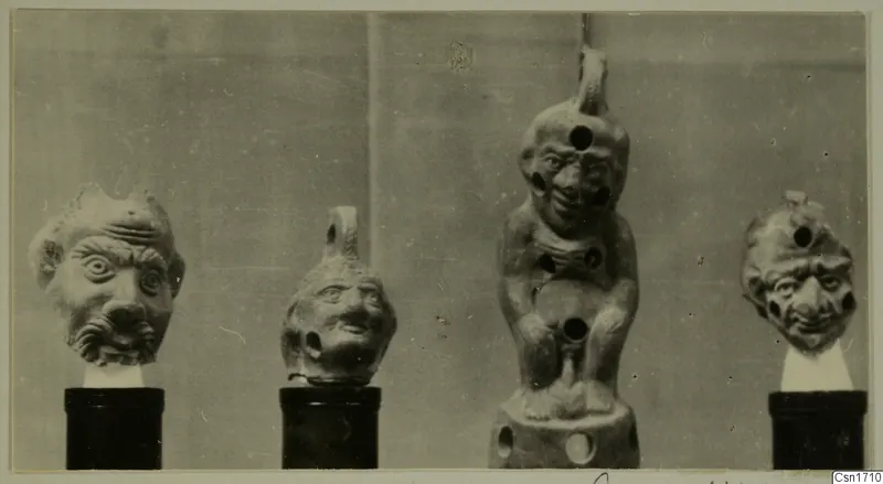 Four small terracotta figures and heads with exaggerated faces, each set on a stand against a grey backdrop.