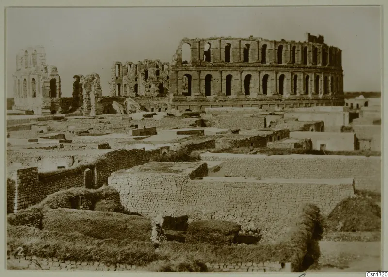 Ruined multi-storey arcaded structure rising above low walls of flat-roofed buildings, North Africa