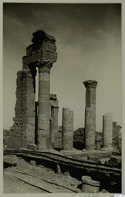 Standing stone columns and low wall ruins with a rail track in the foreground, captioned as North Africa
