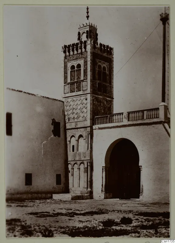 Tall tower with tiled panels beside a whitewashed building with a deep arched doorway