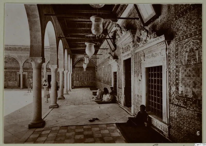 Arcaded courtyard in North Africa with stone columns, patterned tiled walls and several people