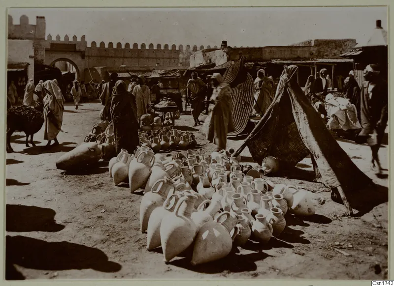 Market scene in North Africa with rows of large pale jars on the ground and people in long robes