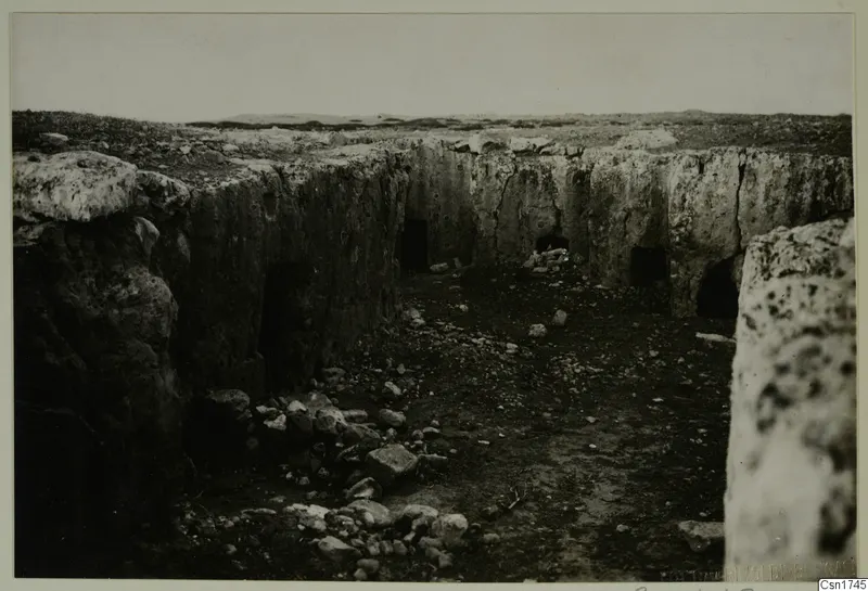 Rock-cut walls with dark openings and recesses in an excavated area, with rubble on the ground in front