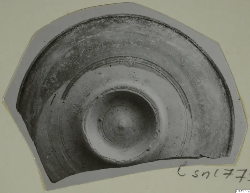 Fragment of a pottery bowl with concentric grooves and a central boss, photographed on grey card.