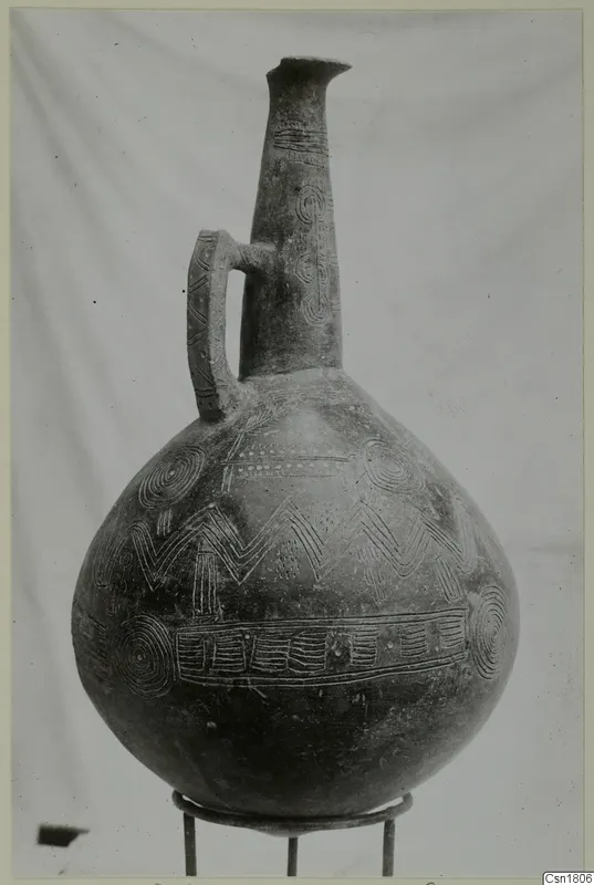 Red Polished III jug from Vounous with incised decoration, standing on a metal ring stand