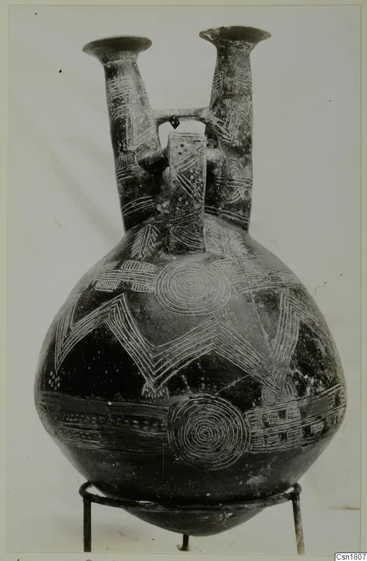 Double-spouted jug from Vounous with white incised zigzag and concentric circle patterns on a dark body.
