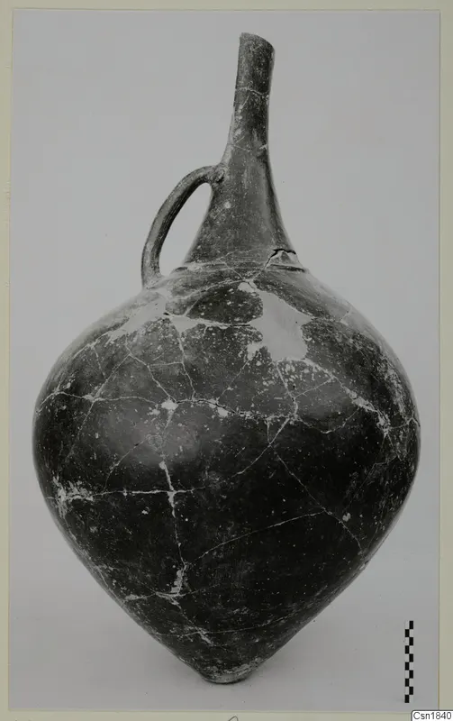 Pottery vessel from Vounous with a long neck and a single loop handle, photographed against a plain backdrop with a scale bar