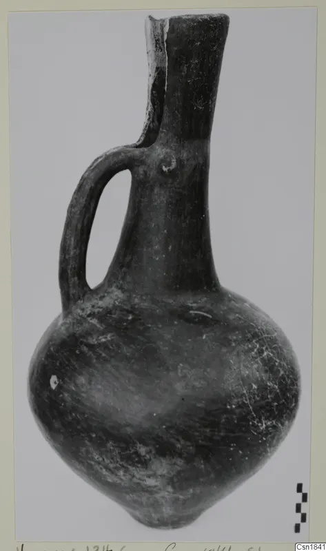 Single-handled polished pottery jug from Vounous, photographed on a grey backdrop beside a scale bar