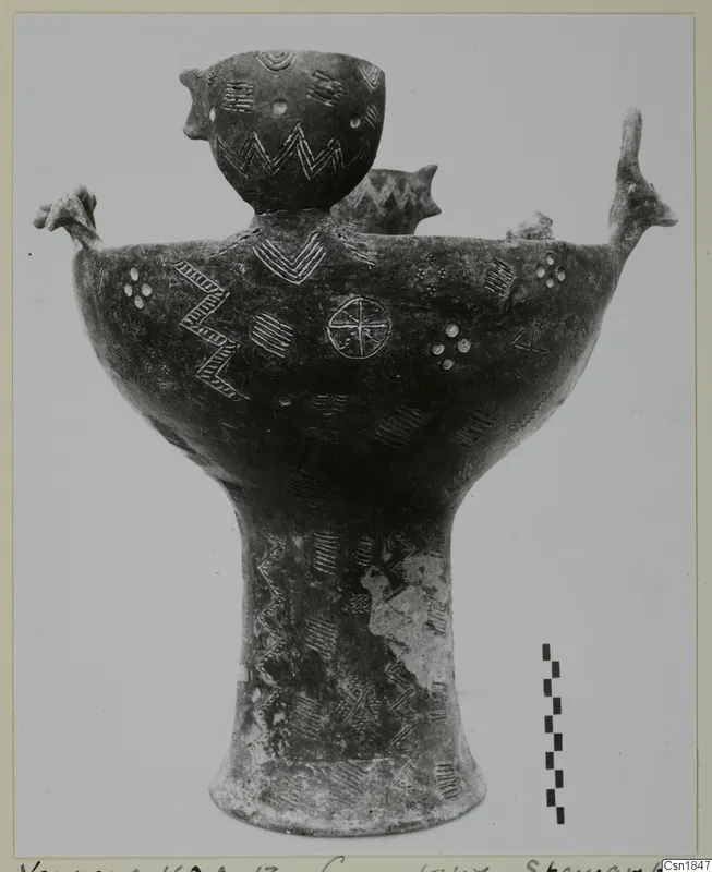 Pottery vessel from Vounous with a tall pedestal foot, incised zigzags and a small cup rising from its body