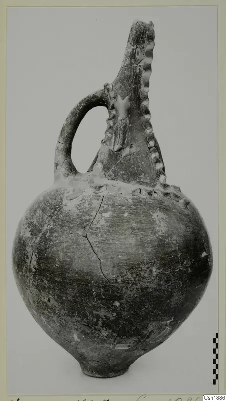 Red Polished I vessel from Vounous with a strap handle and ridged neck, photographed against a plain background.