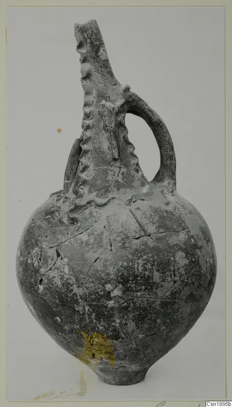 Pottery jug with a tall ridged neck and a single strap handle, photographed against a plain light background.