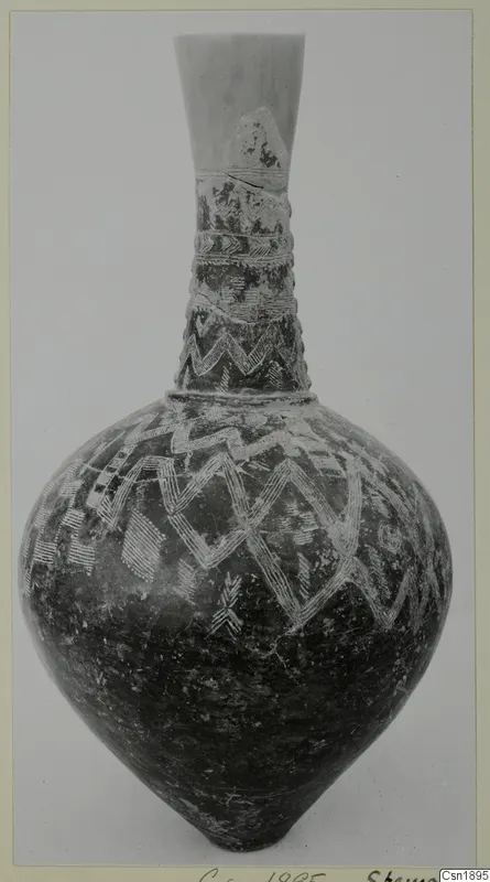 Tall-necked pottery jar with a dark surface and white zigzag and hatched bands, photographed against a plain grey background