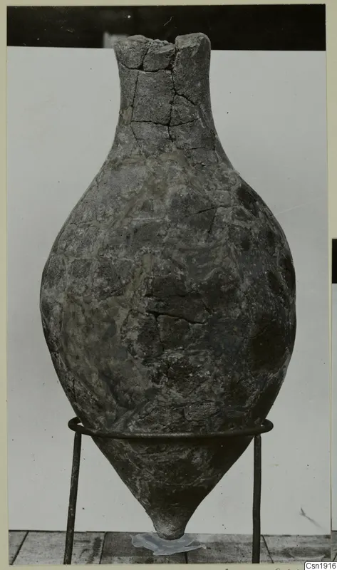 Stone Age pottery vessel with a tall neck and cracked surface, standing on a wire stand