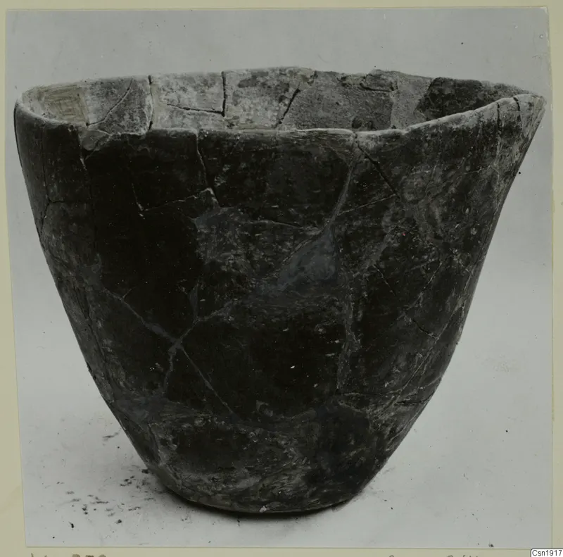 Dark grey bowl with a wide mouth and straight flared sides, its surface cracked and mended, photographed on a plain background.
