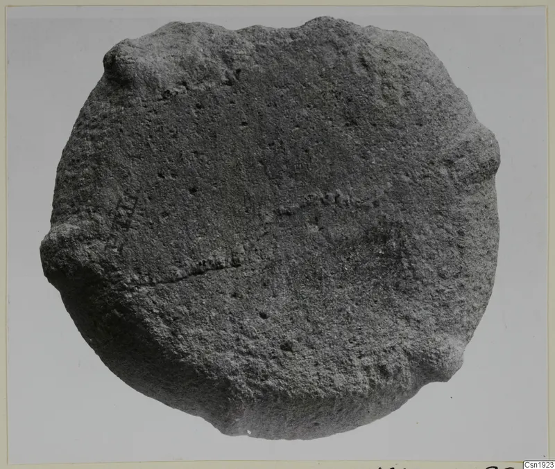 Stone fragment from Petra tou Limniti, roughly round with a rough surface, photographed against a plain grey background.