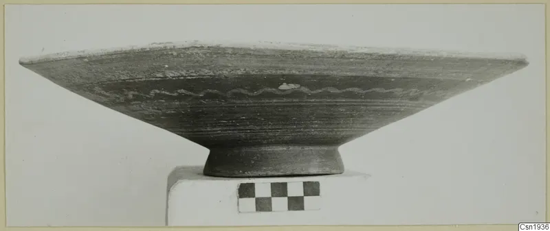 Bichrome-Red pottery bowl with a wavy painted band, photographed on a white plinth beside a checkerboard scale