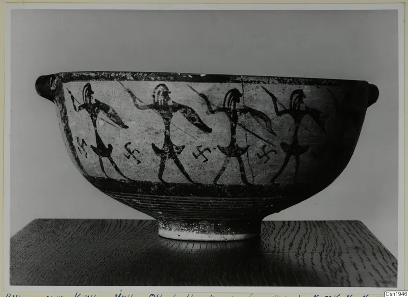 Black-on-Red I-III bowl with painted warriors carrying spears and shields, photographed on a wooden stand