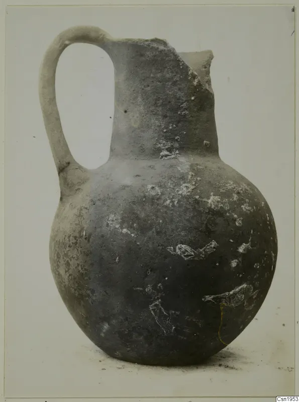 Pottery jug with a tall neck, a broken rim and a loop handle.