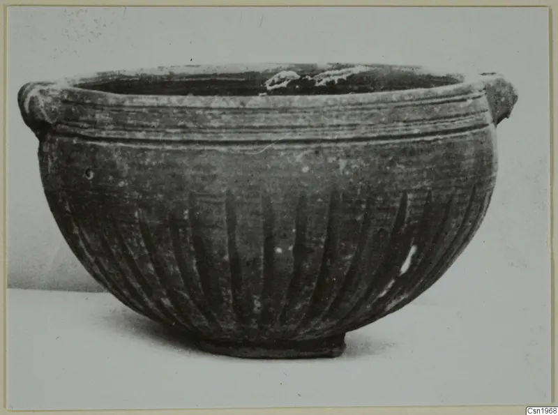 Pottery Black Slip I-VI bowl with two small handles at the rim and vertical grooves on the body