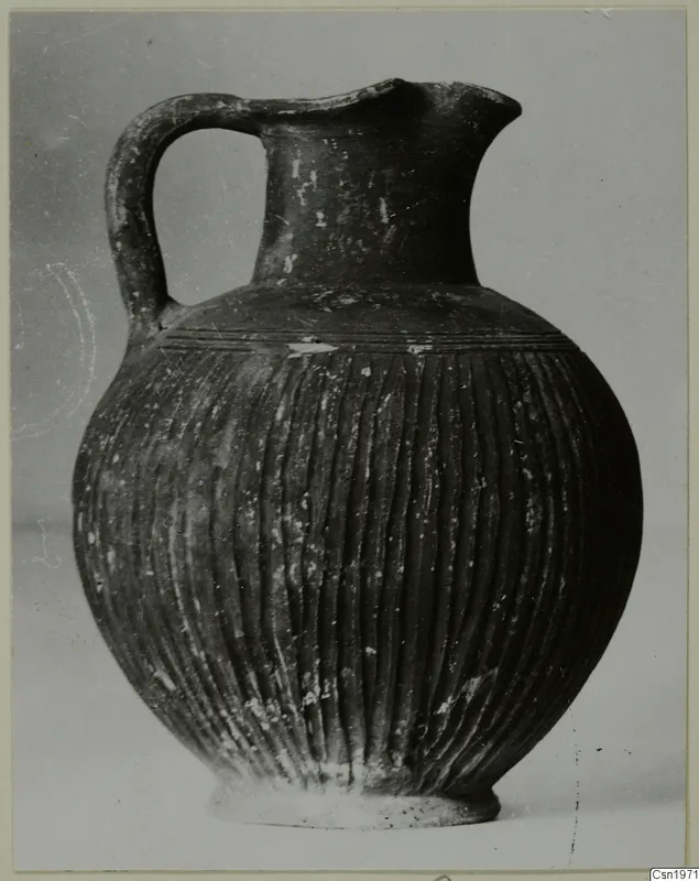Black-slipped jug with a high loop handle and vertical fluting on the body, photographed against a plain background.