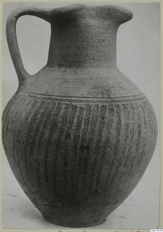 Pottery Black Slip Ware jug with one strap handle and vertical grooves on the body