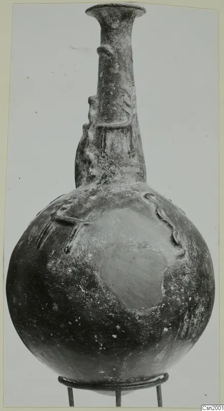 Red Polished II jug from Vounous, with a globular body, tall neck and raised relief decoration, standing on a wire stand.