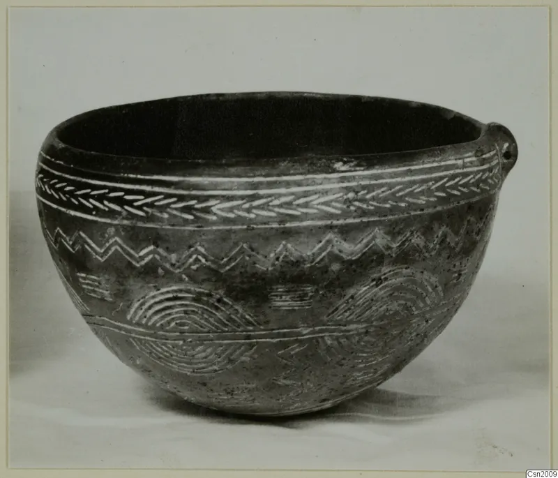 Dark rounded bowl with a small lug on one side and white-filled incised bands of chevron and zigzag decoration, from Lapithos