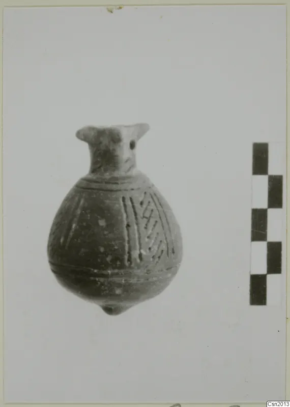 Small pottery vessel with a narrow neck and incised lines on the body, shown beside a scale bar