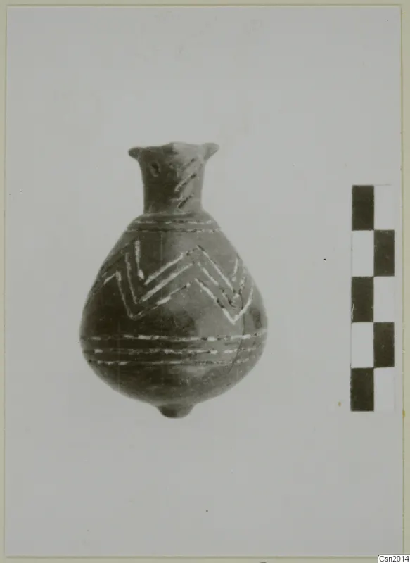 Pottery vessel with a narrow neck and white painted zigzag bands, beside a checkered scale bar