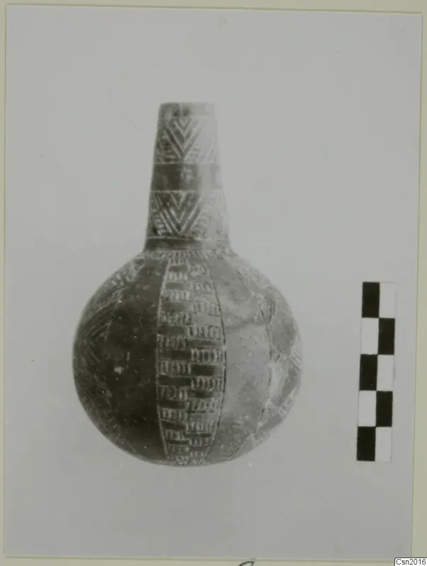 Pottery vessel with a tall narrow neck and incised decoration, shown beside a checkered scale bar