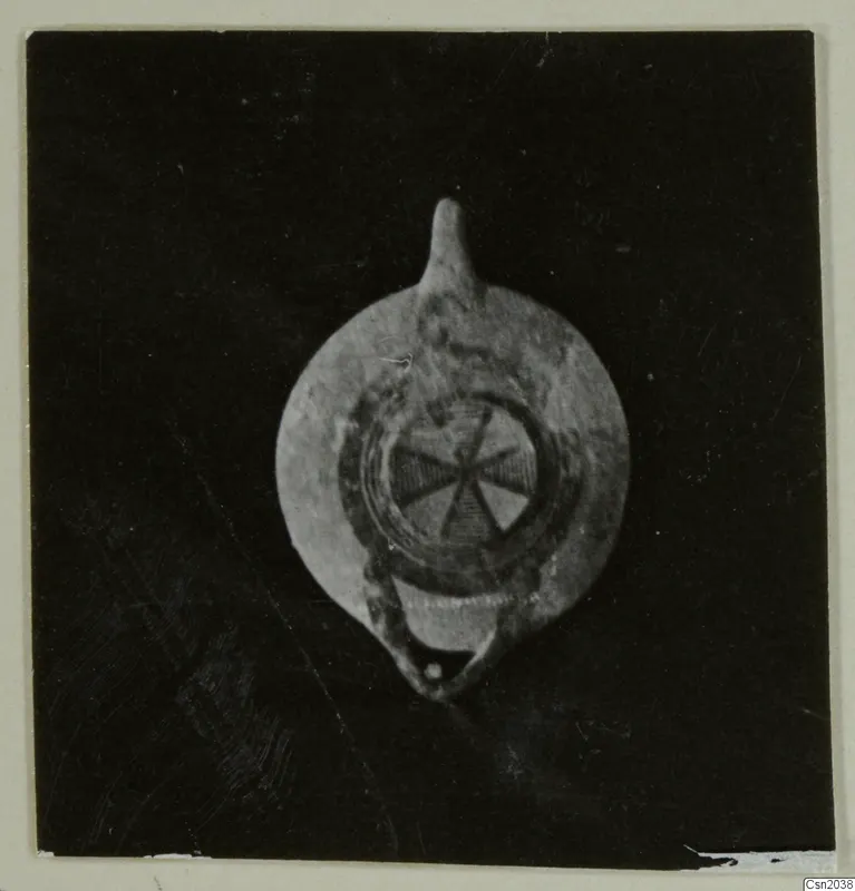 Pottery oil lamp with a nozzle at the top and a radial pattern on its disc, shown against a dark background