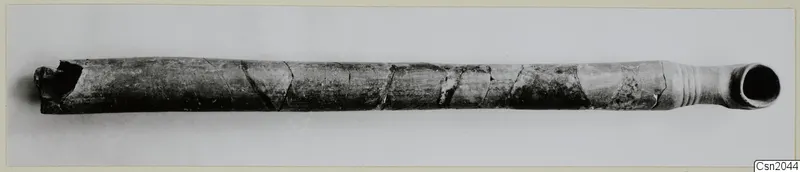 Long tubular object with a flared mouth at one end, dark grey surface with cracks, lying horizontally on a pale background
