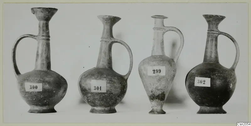 Four pottery Base Ring jugs with single handles, standing in a row with number labels