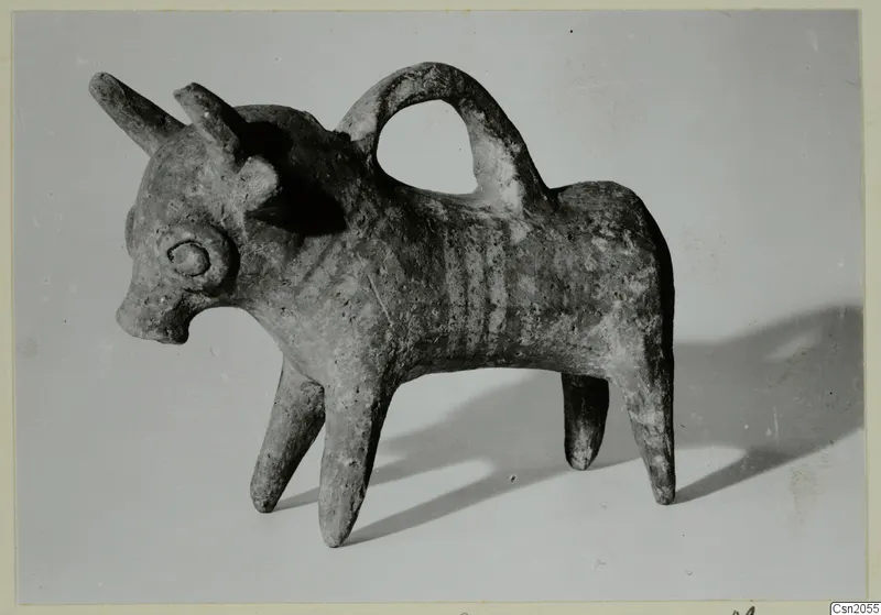 Pottery vessel modelled as a horned animal with a looped handle over its back, shown on a plain grey backdrop