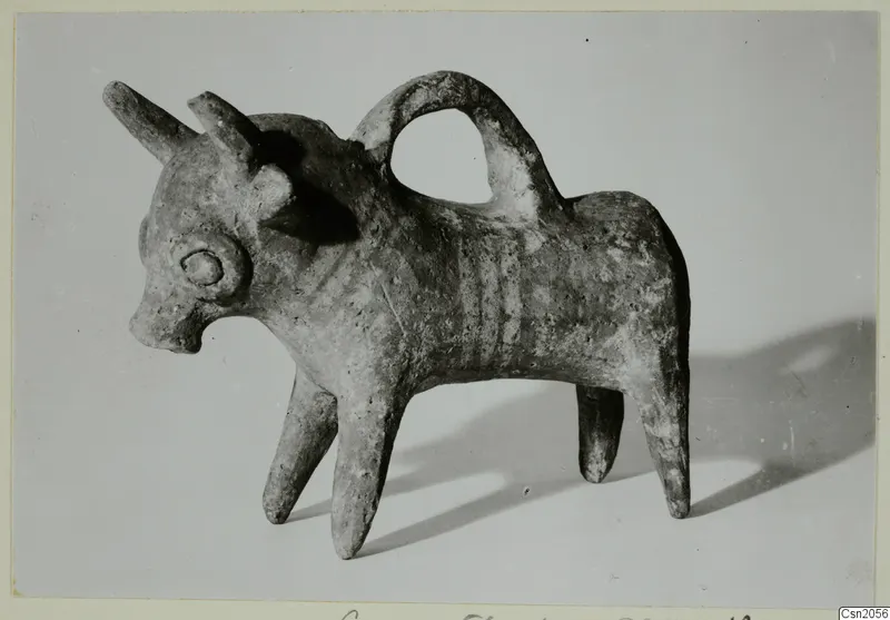 Clay bull-shaped vessel with a loop handle over its back, photographed against a pale grey background.