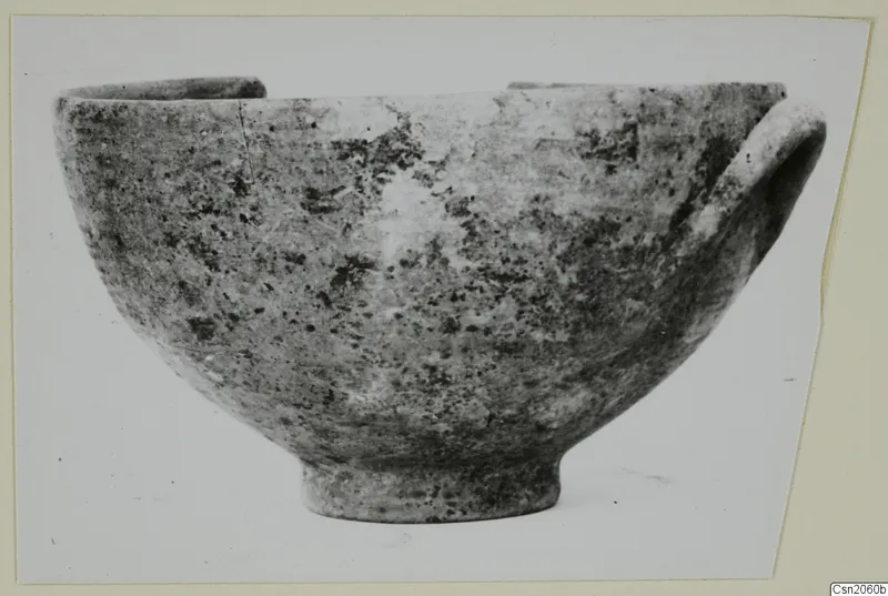 Bowl with a rounded body, ring foot and a handle on its right side, photographed against a pale background