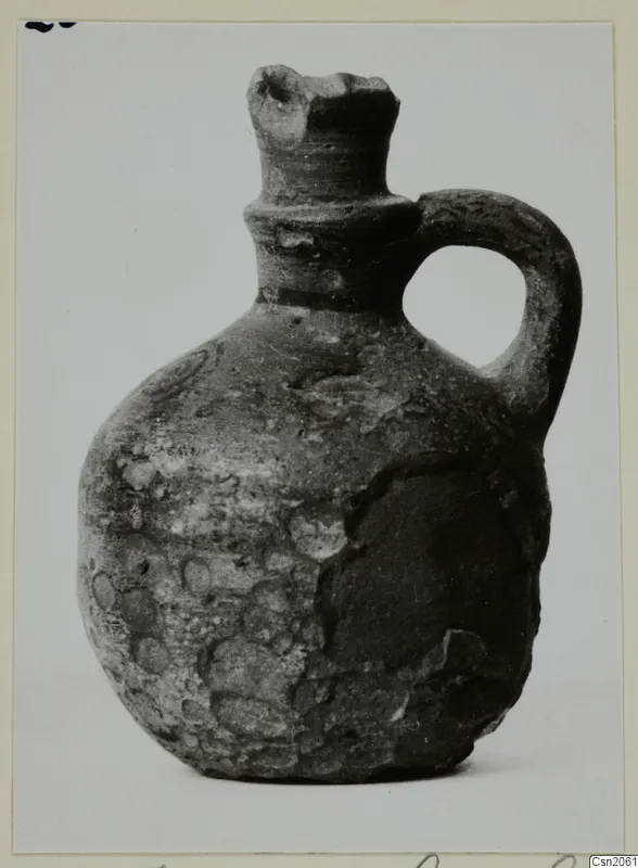 Small jug with a single loop handle and a broken rim, photographed against a plain background.